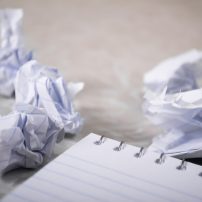 内容撰写编辑伏案写作的近景，笔记本上贴着几张彩色便签，旁边摊着宫原前辈和藤原后辈 漫画条目的改写草稿